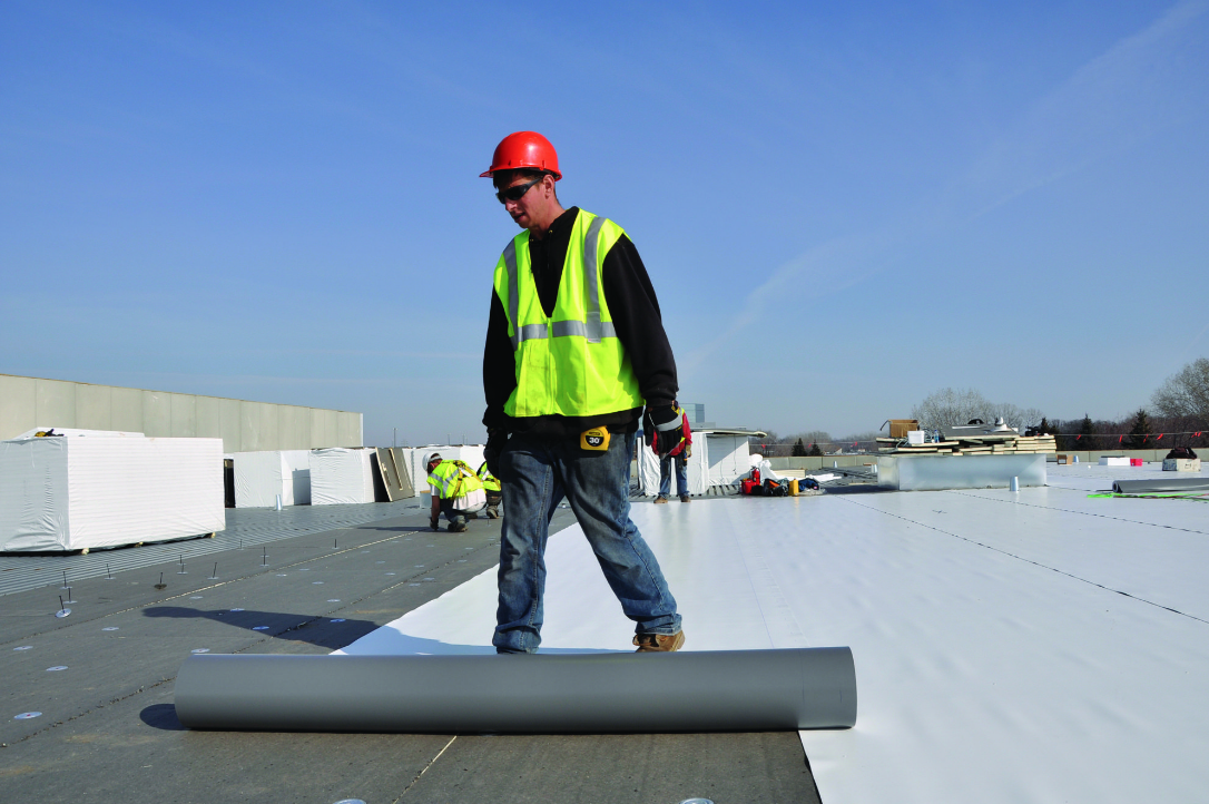 Crew member rolling out roof coating.